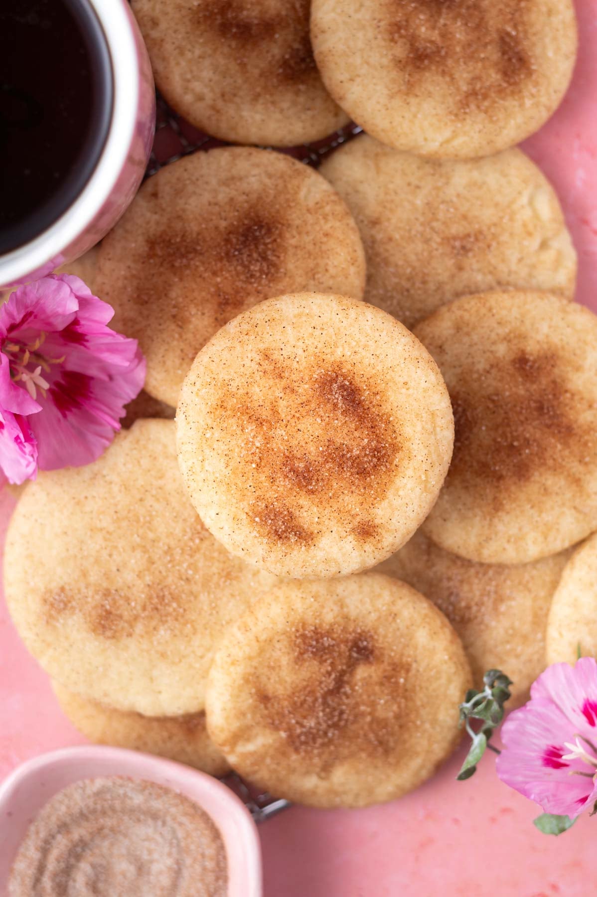 over head look at a pile of snickerdoodle cookies with a cup of coffee and a bowl of cinnamon sugar