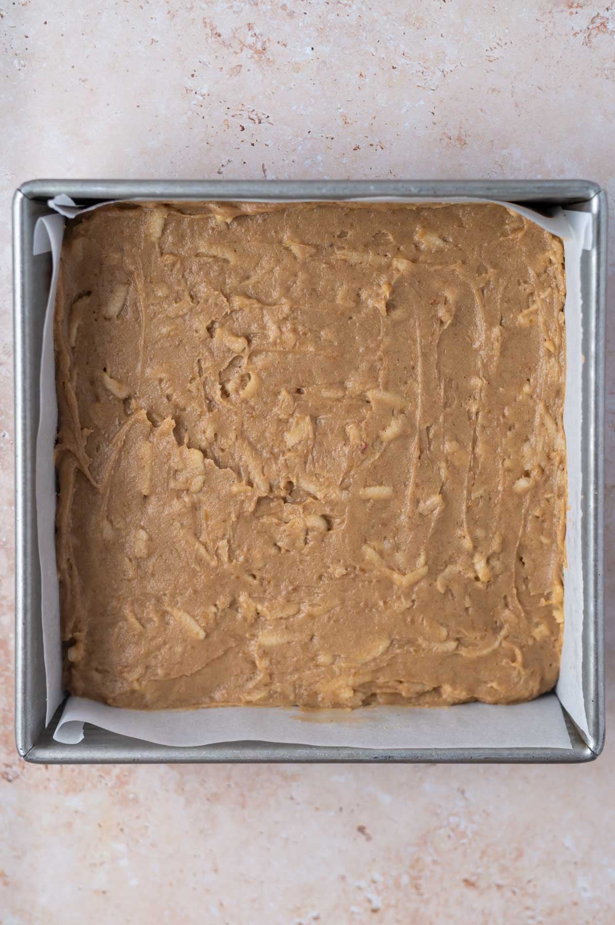 apple cinnamon blondie batter in a parchment lined baking tin
