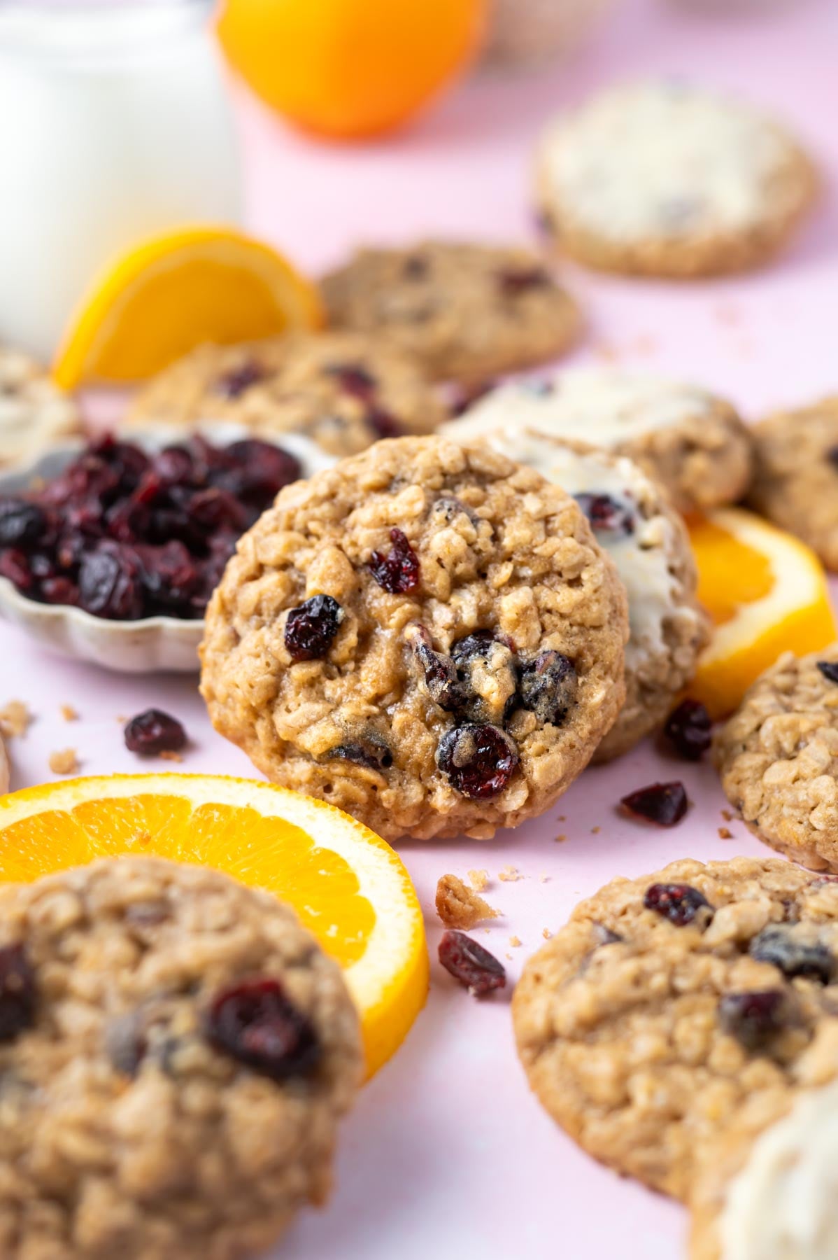 orange cranberry oatmeal cookies with orange slices and a glass of milk in the background