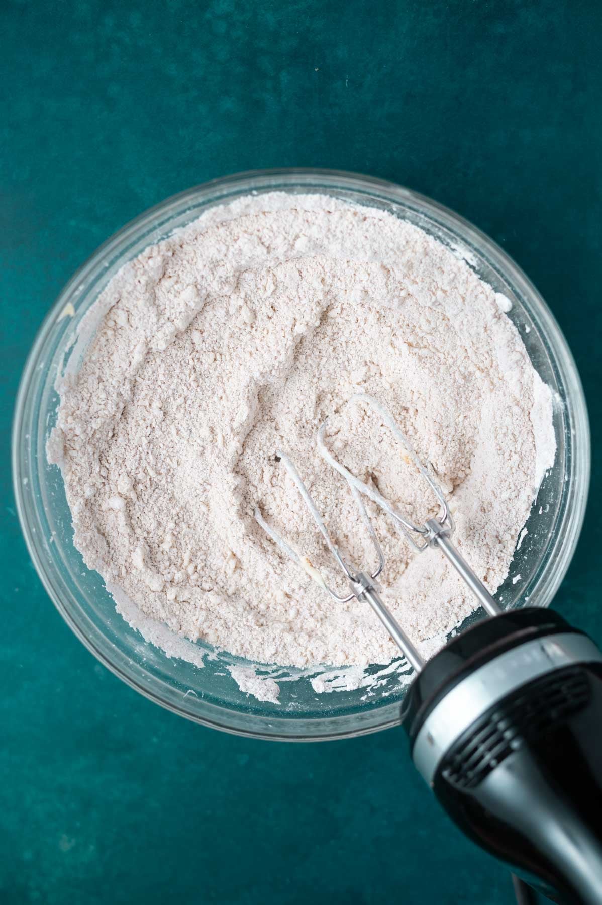 confectioners sugar and butter mixture looking like sand in a glass mixing bowl