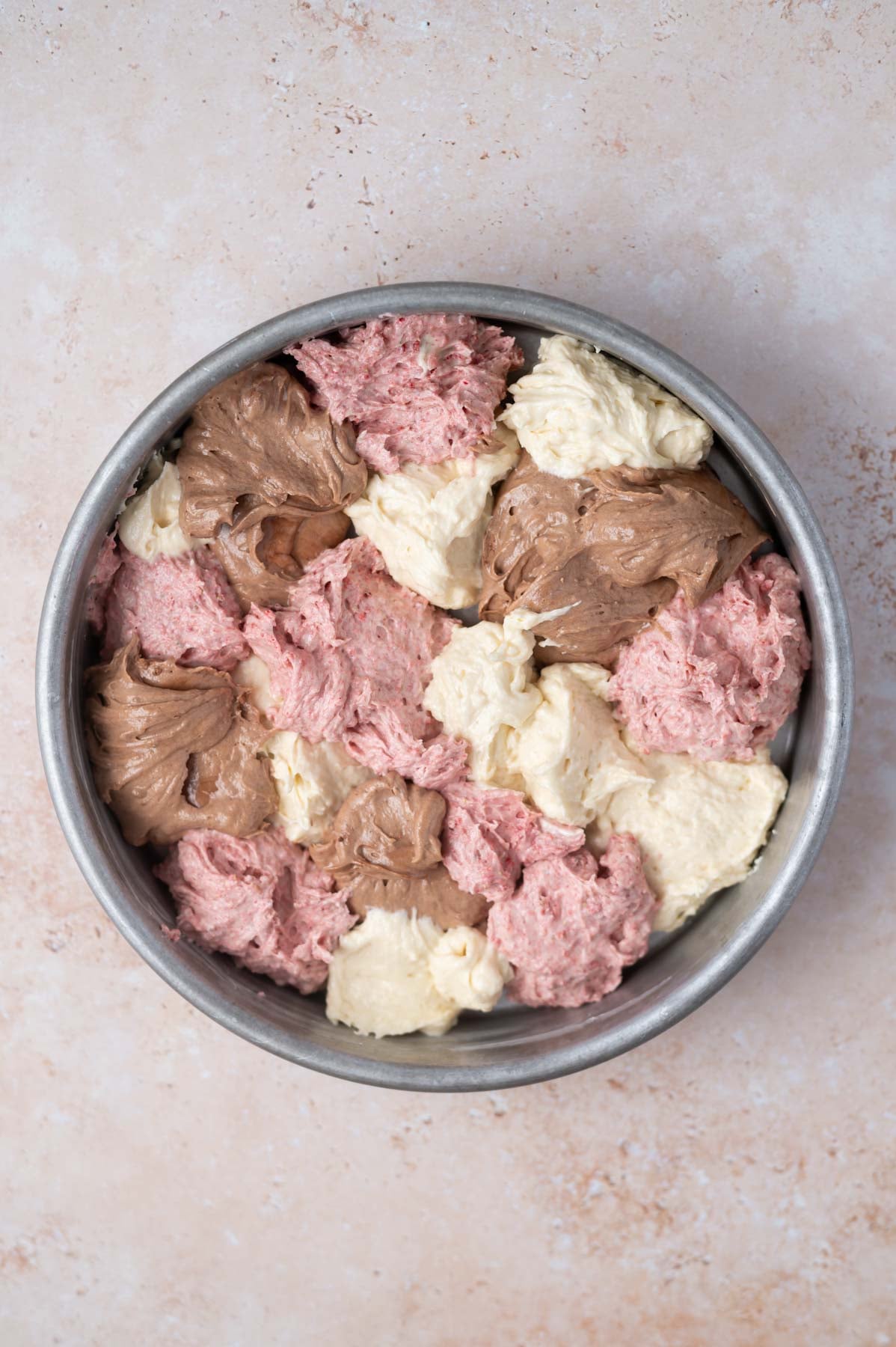 scoops of vanilla, strawberry, and chocolate cake batter in a round baking tin