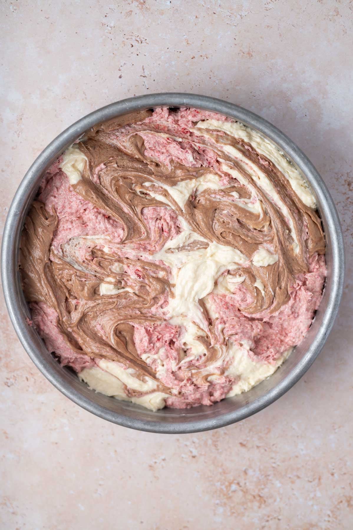 chocolate, strawberry, and vanilla batters swirled together in a baking pan