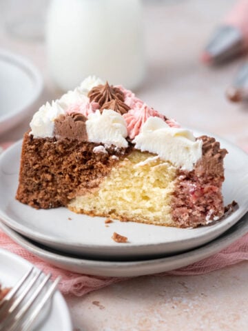 slice of neapolitan cake on a plate with a glass of milk and piping bags of frosting in the background