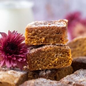 a stack of pumpkin blondies with a purple flower and milk in the background