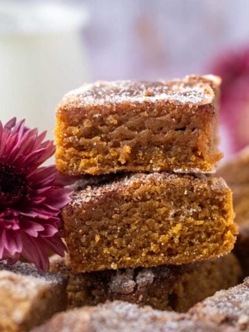 a stack of pumpkin blondies with a purple flower and milk in the background