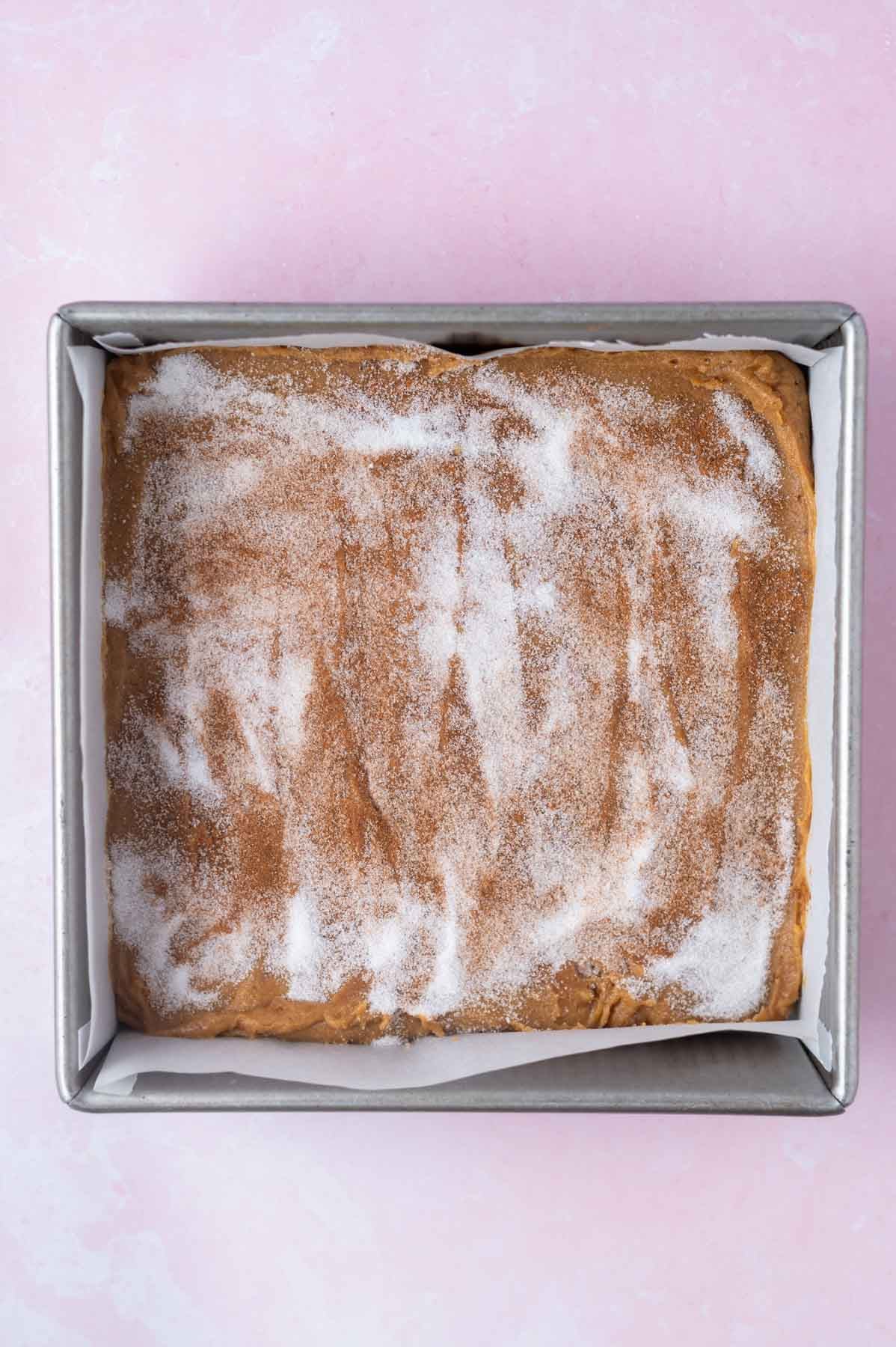cinnamon sugar topping sprinkled over dough in a parchment lined baking pan