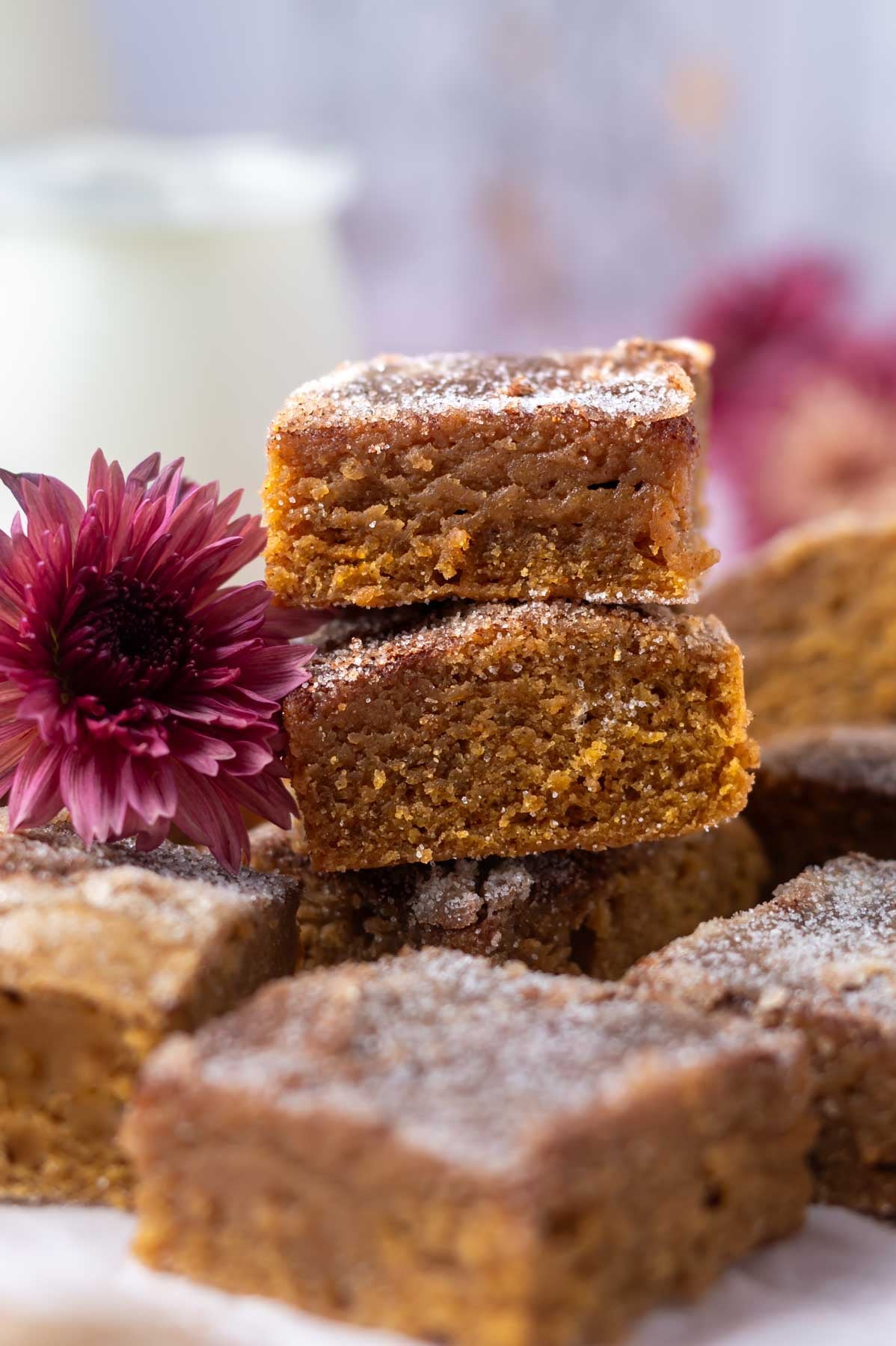 a stack of pumpkin blondies with a purple flower and milk in the background
