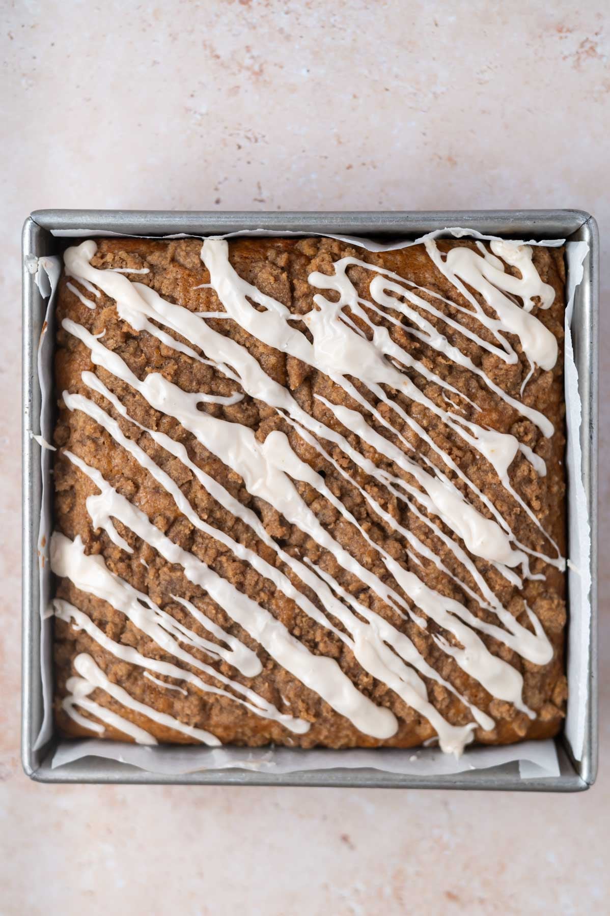 icing drizzled over baked coffee cake in a parchment lined pan
