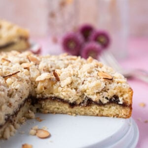 almond coffee cake on a plate with slices missing and fresh flowers in the background