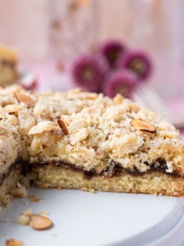 almond coffee cake on a plate with slices missing and fresh flowers in the background