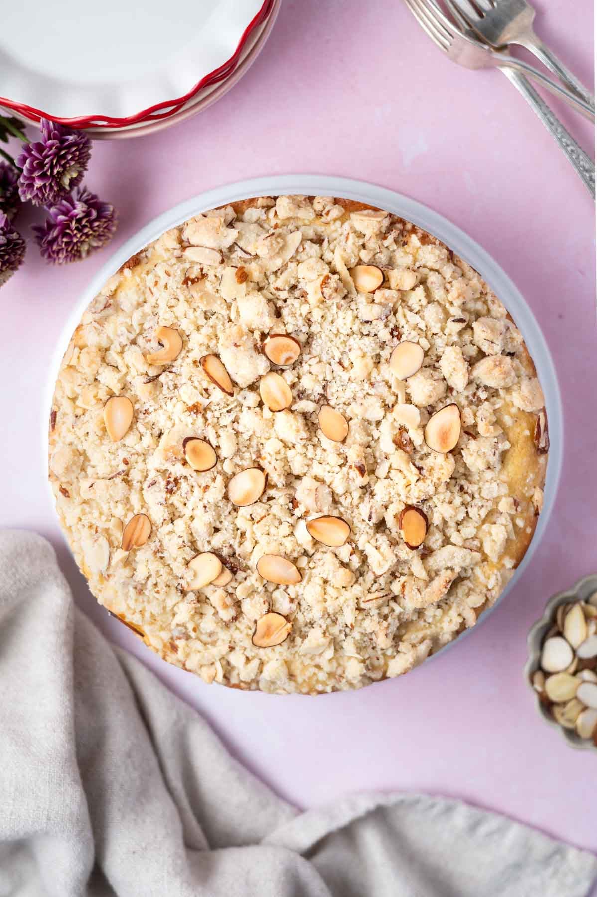 baked almond coffee cake with streusel and extra almond slices on top with plates, forks and a napkin