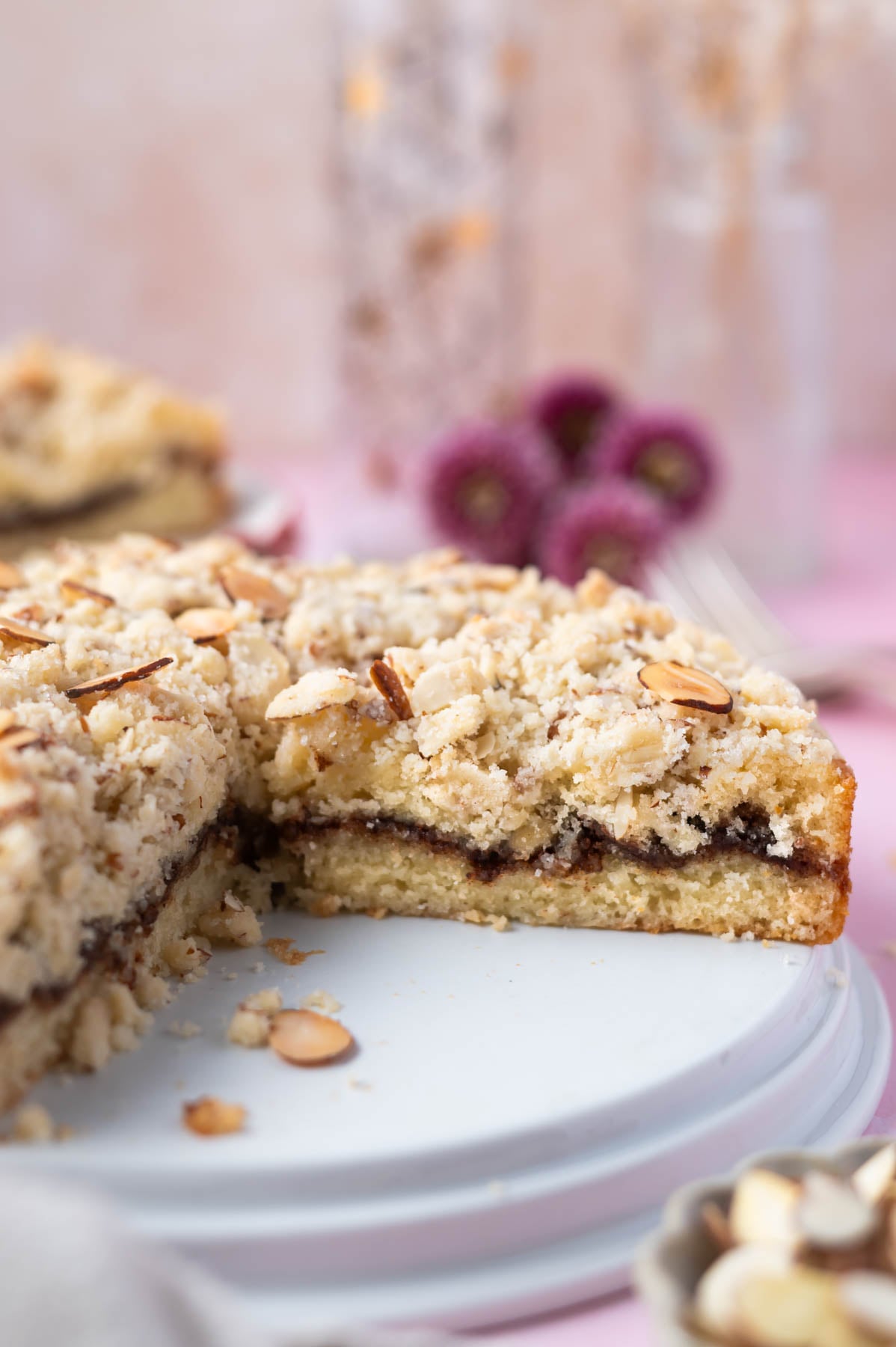 almond coffee cake on a plate with slices missing and fresh flowers in the background