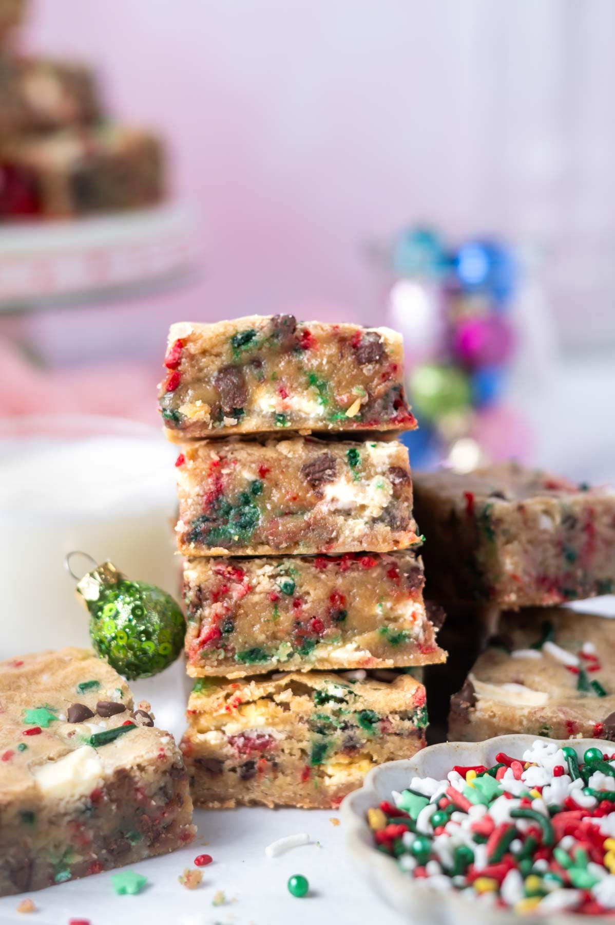 stack of Christmas blondies with a glass of milk and bowl of sprinkles in the foreground