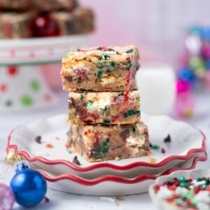 stack of Christmas blondies on a plate with sprinkles in the foreground and milk in the background