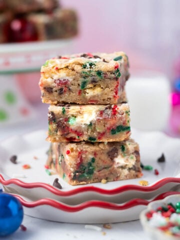 stack of Christmas blondies on a plate with sprinkles in the foreground and milk in the background