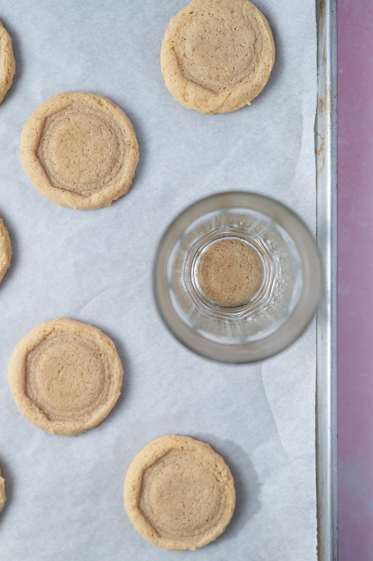 baked cookies on a parchment lined pan with a glass flattening one of them