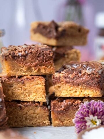 stack of blondies with a glass of milk, jar of Nutella in the background and fresh flowers